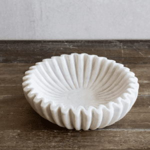 White ceramic bowl with a fluted, scalloped edge on a wooden surface.